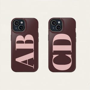 May include: Two maroon phone cases with a pink monogram. One case displays the letters "AB" and the other displays "CD". The cases have a dark camera lens and a smooth finish.