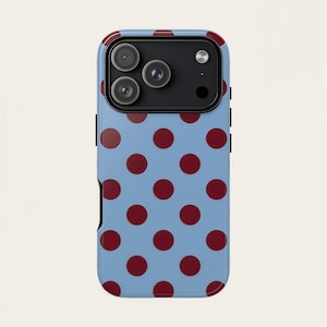 May include: A light blue phone case with a repeating pattern of large, dark red polka dots. The case has a black border and a camera cutout at the top. The phone case is designed to fit a smartphone.