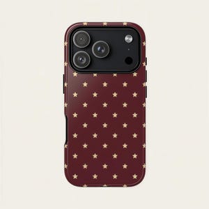 May include: A burgundy phone case with a repeating pattern of small, gold stars. The case has a black camera module with three lenses and a flash. The case is designed to fit a smartphone.