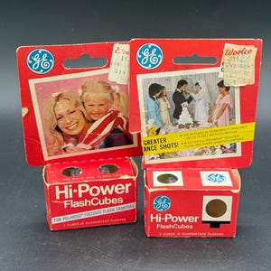 May include: Vintage GE Hi-Power FlashCubes for Polaroid cameras. Two red boxes with white text and the GE logo. The packaging includes images of a mother and child, and a wedding. The boxes contain 2 cubes and 8 guaranteed flashes.