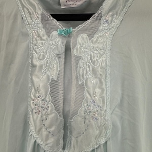 May include: A light blue Vanity Fair nightgown. The nightgown features a delicate lace and mesh neckline with floral embroidery and a small bow. The tag reads "Vanity Fair MADE IN U.S.A."