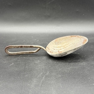 Puede incluir: Cuchara metálica vintage con un cuenco redondeado y un asa en forma de lazo. La cuchara tiene un aspecto desgastado y envejecido. El asa tiene grabado el texto "BRIGHTE BRASS" y "H.R. HARP". Probablemente se utiliza para medir o recoger.