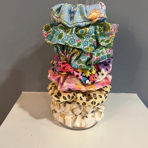 May include: A stack of colorful fabric scrunchies in a variety of patterns, including floral, geometric, and animal print.