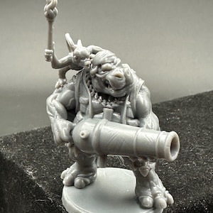 May include: A gray miniature figurine of a fantasy creature with a cannon and a small figure holding a torch. The creature has a reptilian appearance with detailed armor and a round base. The torch is held high above the creature's head.