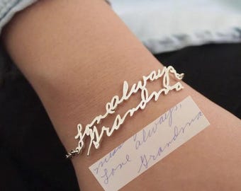 May include: A silver bracelet with the words "forever always" written in cursive. The bracelet is on a person's wrist. A handwritten note on a white piece of paper says "miss you always, love Grandma".