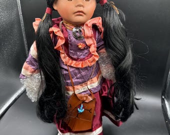 Muñeca coleccionable de porcelana de estilo nativo americano con cabello largo negro, ojos marrones y un atuendo granate y naranja.