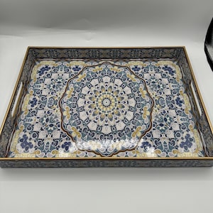May include: A rectangular serving tray with a gold-toned frame and integrated side handles. The interior surface features a detailed, symmetrical mandala-inspired pattern in shades of navy blue, light blue, cream, and muted gold.