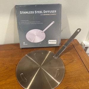 May include: A stainless steel diffuser with a separable handle, designed to protect surfaces. The product is in its original packaging, which includes the text "STAINLESS STEEL DIFFUSER with SEPARABLE HANDLE". The diffuser is circular with a handle attached.