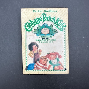 May include: A rectangular Cabbage Patch Kids card game box by Parker Brothers. The front features the green logo, a cabbage illustration, and three characters. Text reads: Cabbage Patch Kids, Card Game, Make New Friends, 3 Games in 1.