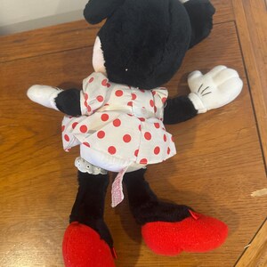 Puede incluir: Una mu&ntilde;eca de peluche de Minnie Mouse, con pelo negro, guantes blancos y zapatos rojos. Viste un vestido blanco con lunares rojos y un lazo a juego. Un juguete cl&aacute;sico para ni&ntilde;os.