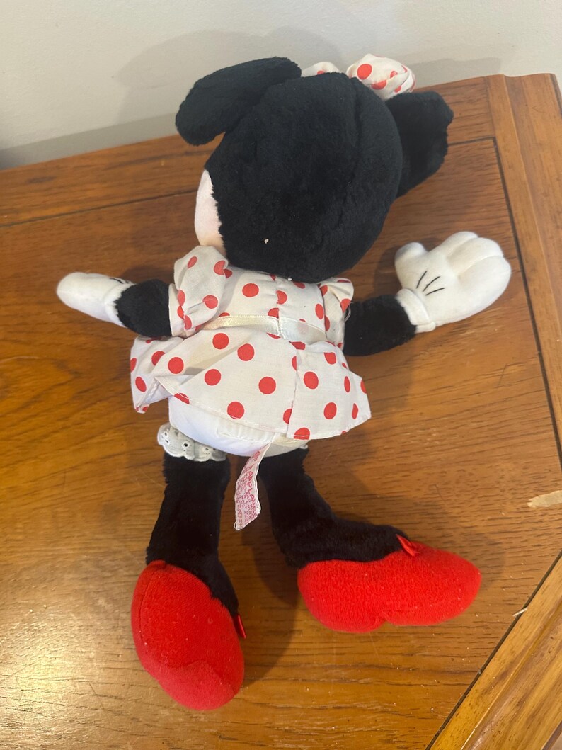 Puede incluir: Una mu&ntilde;eca de peluche de Minnie Mouse, con pelo negro, guantes blancos y zapatos rojos. Viste un vestido blanco con lunares rojos y un lazo a juego. Un juguete cl&aacute;sico para ni&ntilde;os.