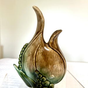 May include: A ceramic vase in the shape of a stylized flower bud. The vase features a gradient of colors, transitioning from green at the base to brown at the top. The design includes textured details and a glossy finish.
