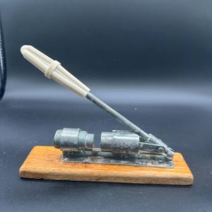 May include: A vintage nutcracker with a wooden base, metal components, and a cream-coloured handle. The nutcracker has a lever-style design and is designed to crack nuts. The metal components show signs of wear, adding to its antique charm.