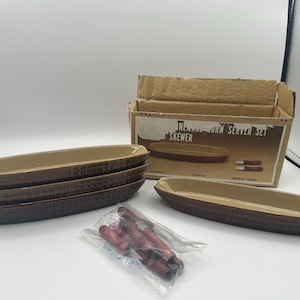 May include: A set of brown ceramic corn-shaped serving dishes with a textured exterior and a tan interior. The set includes a box labeled "Newware Corn Server Set" and a package of skewers.