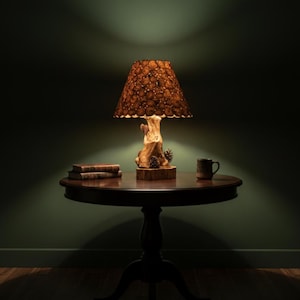 Può includere: Una lampada da tavolo rustica con base a tronco d'albero e paralume a fette di legno. La lampada è su un tavolo di legno scuro con libri e una tazza. La lampada è accesa, creando un'atmosfera calda.