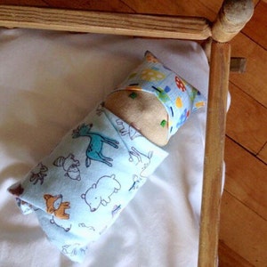 May include: A blue and white fabric doll with a brown head and a blue and yellow patterned pillow. The doll is lying in a wooden crib.