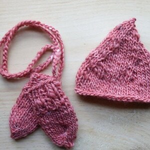 May include: A set of pink knitted baby booties and a matching hat. The booties are attached to a long cord, making them a unique and charming gift.