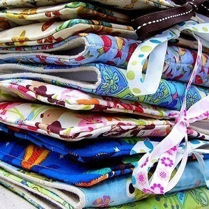 May include: A vertical stack of folded fabric pouches featuring various colorful patterns including floral, animal, and geometric prints. Each pouch is secured with a decorative ribbon tied in a bow, showcasing a mix of blue, pink, green, and cream tones.