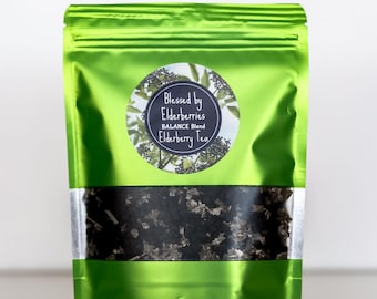 May include: A green resealable pouch with a white label that reads "Blessed by Elderberries BALANCE Blend Elderberry Tea". The label has a black circle with a picture of elderberries. The pouch contains dried elderberries.