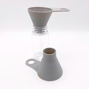 May include: A clear plastic bottle with a gray funnel inserted in the opening. Another gray funnel is next to the bottle. Both funnels have a handle. The funnels are designed to help fill the bottle.