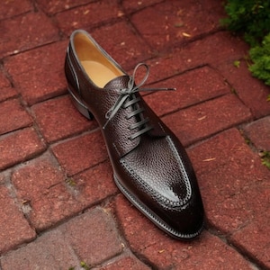 May include: A brown leather lace-up dress shoe with a pointed toe and a textured finish.