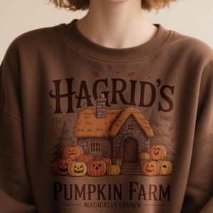 May include: Brown sweatshirt featuring a graphic of a cottage with pumpkins and the text "Hagrid's Pumpkin Farm". The design includes the text "EST 1981" and "Magically Grown".