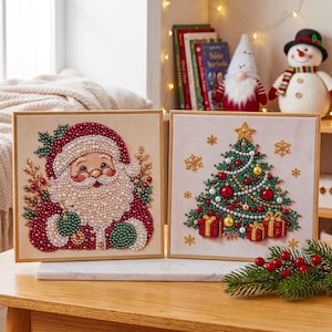Könnte beinhalten: Zwei quadratische Wandbilder mit perlenbesetzten Weihnachtsmotiven. Eine Leinwand zeigt einen Weihnachtsmann mit einem Bart aus weißen Perlen und einer roten Mütze. Die andere Leinwand zeigt einen grünen Weihnachtsbaum mit rotem und goldenem Schmuck.