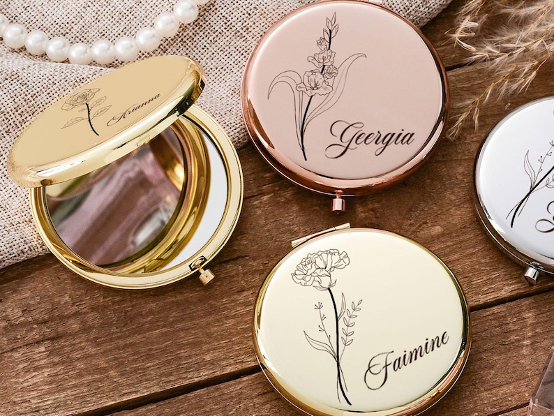 May include: A collection of personalized compact mirrors in gold, rose gold, and silver. Each mirror features a floral design and a name, such as "Arianna" and "Georgia", engraved on the surface. The open gold mirror reveals a reflective surface.