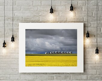 Canola Farmers Field with Grain Silos Stormy Skies by Mountains