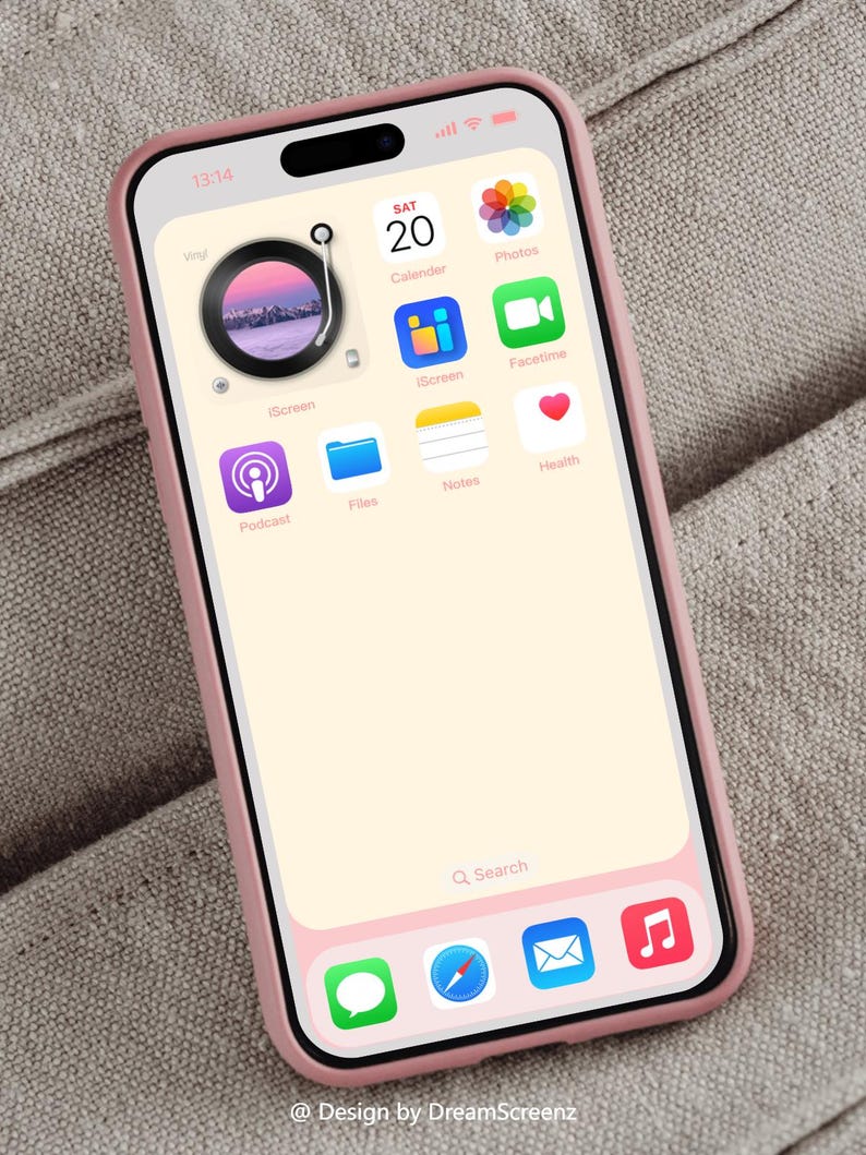 Op de afbeelding: Een roze smartphone met een zwarte rand en een lichtroze hoesje. Het scherm toont app-iconen, waaronder Agenda, Foto's en FaceTime. De achtergrond van de telefoon heeft een platenspelerontwerp. De tijd is 13:14 uur.