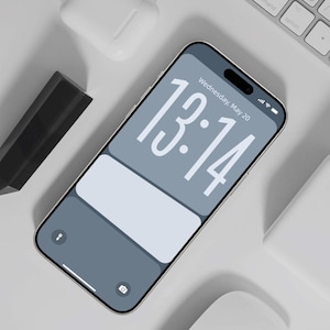 Könnte beinhalten: Ein Smartphone mit einem hellblauen Bildschirm, der die Uhrzeit 13:14 anzeigt, mit einem hellblauen und weißen Hintergrund. Das Telefon ist umgeben von einer weißen Tastatur, einer weißen Maus, einem weißen Ladecase und einem schwarzen Stift. Der Text "Wednesday, May 20" ist sichtbar.