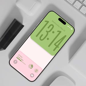 以下が含まれることがあります： 13時14分と天気情報を表示する緑とピンクのディスプレイを備えたスマートフォン。 白いキーボード、ワイヤレスイヤホン、黒いスタイラスに囲まれています。 画面には「Wednesday, May 20」と表示されています。 テキスト「@ Design by DreamScreenz」が下にあります。