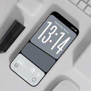 Może przedstawiać: Smartfon z szarym i białym ekranem wyświetlającym godzinę 13:14 i datę środa, 20 maja. Telefon znajduje się obok białej klawiatury, bezprzewodowych słuchawek i czarnego rysika. Ekran pokazuje prognozę deszczu 50%.