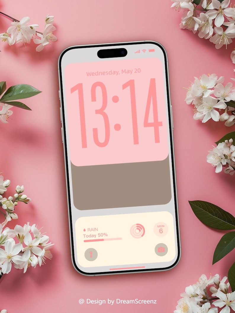Op de afbeelding: Een smartphonescherm toont de tijd 13:14 in roze, met een roze en bruin kleurenschema. Het scherm toont ook de datum, weersinformatie en een camera-icoon. Witte bloemen en groene bladeren zijn rond de telefoon gerangschikt op een roze achtergrond. De tekst "@ Design by DreamScreenz" staat onderaan.
