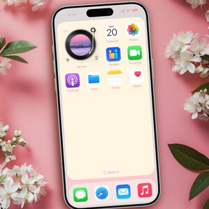 Op de afbeelding: Een smartphonescherm toont een aangepast startscherm met app-pictogrammen, waaronder Agenda, Foto's en Gezondheid. De achtergrond is zachtroze, met witte bloemen en groene bladeren in de hoeken. De tijd is 13:14. De tekst "@ Design by DreamScreenz" staat onderaan.