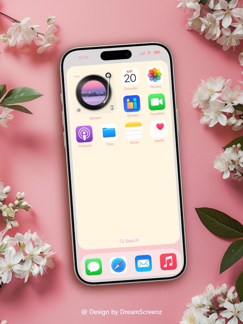 Op de afbeelding: Een smartphonescherm toont een aangepast startscherm met app-pictogrammen, waaronder Agenda, Foto's en Gezondheid. De achtergrond is zachtroze, met witte bloemen en groene bladeren in de hoeken. De tijd is 13:14. De tekst "@ Design by DreamScreenz" staat onderaan.