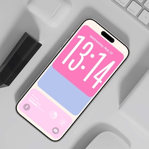 May include: A smartphone with a pink and blue lock screen showing the time 13:14 and the date Wednesday, May 20. The phone is next to a white keyboard, wireless earbuds, a black stylus, and a white mouse. The screen displays the battery level.