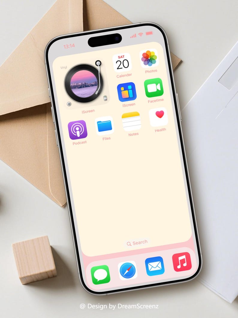 Op de afbeelding: Een smartphone scherm toont een aangepast startscherm met een vinyl record widget, kalender en app iconen. De achtergrond is een zachte perzikkleur met een roze rand. De tijd is 13:14. Design by DreamScreenz.