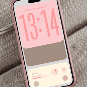 Op de afbeelding: Een roze smartphone in een lichtroze hoesje toont een aangepast vergrendelscherm. Het scherm toont de tijd 13:14 in roze, met een weerwidget die 50% kans op regen aangeeft. De datum is woensdag 20 mei. Ontwerp door DreamScreenz.