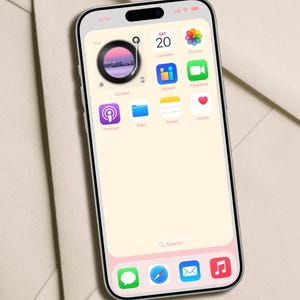 Op de afbeelding: Een smartphone met een lichtroze en wit scherm toont app-iconen, waaronder een kalender, foto's en een podcast-app. Het scherm toont de tijd als 13:14. De telefoon heeft een zwart camera-gedeelte aan de bovenkant en een roze onderrand. Design by DreamScreenz.
