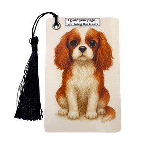 May include: Bookmark featuring a Cavalier King Charles Spaniel illustration. The dog is depicted with brown and white fur, large eyes, and a sweet expression. The bookmark has a black tassel and the text: "I guard your page... you bring the treats."