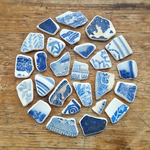May include: A collection of blue and white ceramic shards arranged in a circular pattern on a wooden surface. The shards feature various patterns and designs, including floral and geometric motifs. The color palette is primarily blue and white.