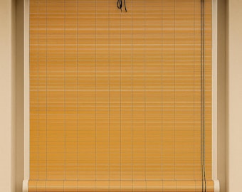 May include: A handwoven bamboo blind featuring a natural tan color with a grid pattern. The top section has a blue fabric header with the white text HANDWOVEN BAMBOO BLIND. A black pull cord hangs down the right side to adjust the roll-up mechanism.