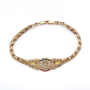 May include: Gold-toned bracelet featuring a central religious emblem with colorful accents. The bracelet has a floral design with small, sparkling embellishments. The clasp is visible, and the bracelet is set against a white background.