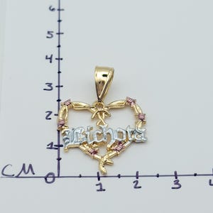 May include: A gold heart pendant with the word "Bichota" in silver lettering. The heart is decorated with pink accents and a bow. The pendant is approximately 1.5 cm wide.