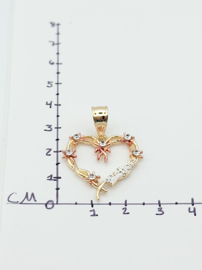 May include: A gold-toned heart pendant with a 'Mother' inscription. The heart is adorned with small, clear gemstones and rose gold accents. The pendant is approximately 1.5 cm wide.
