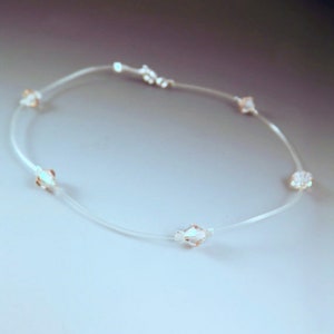 Peut inclure: Collier délicat avec un fil transparent, presque invisible, orné de perles de cristal scintillantes et facettées. Le collier a un fermoir simple. Les cristaux semblent flotter. Les cristaux sont d'une couleur claire et irisée.