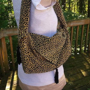 May include: A brown and black leopard print shoulder bag with black tassels. The bag is made of a soft, fabric material.