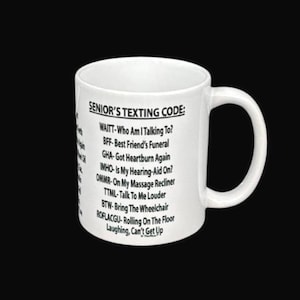 Könnte beinhalten: Weiße Keramik-Tasse mit dem Text "SENIOR'S TEXTING CODE:" und einer Liste von SMS-Abkürzungen. Die Tasse hat einen gebogenen Henkel und steht vor einem schwarzen Hintergrund.