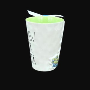 Puede incluir: Taza de cer&aacute;mica blanca con interior verde claro y exterior texturizado. La taza presenta el texto "AW YOUR SISTER" en letras negras y una peque&ntilde;a ilustraci&oacute;n de extraterrestres verdes. Una cinta blanca est&aacute; atada alrededor de la parte superior.